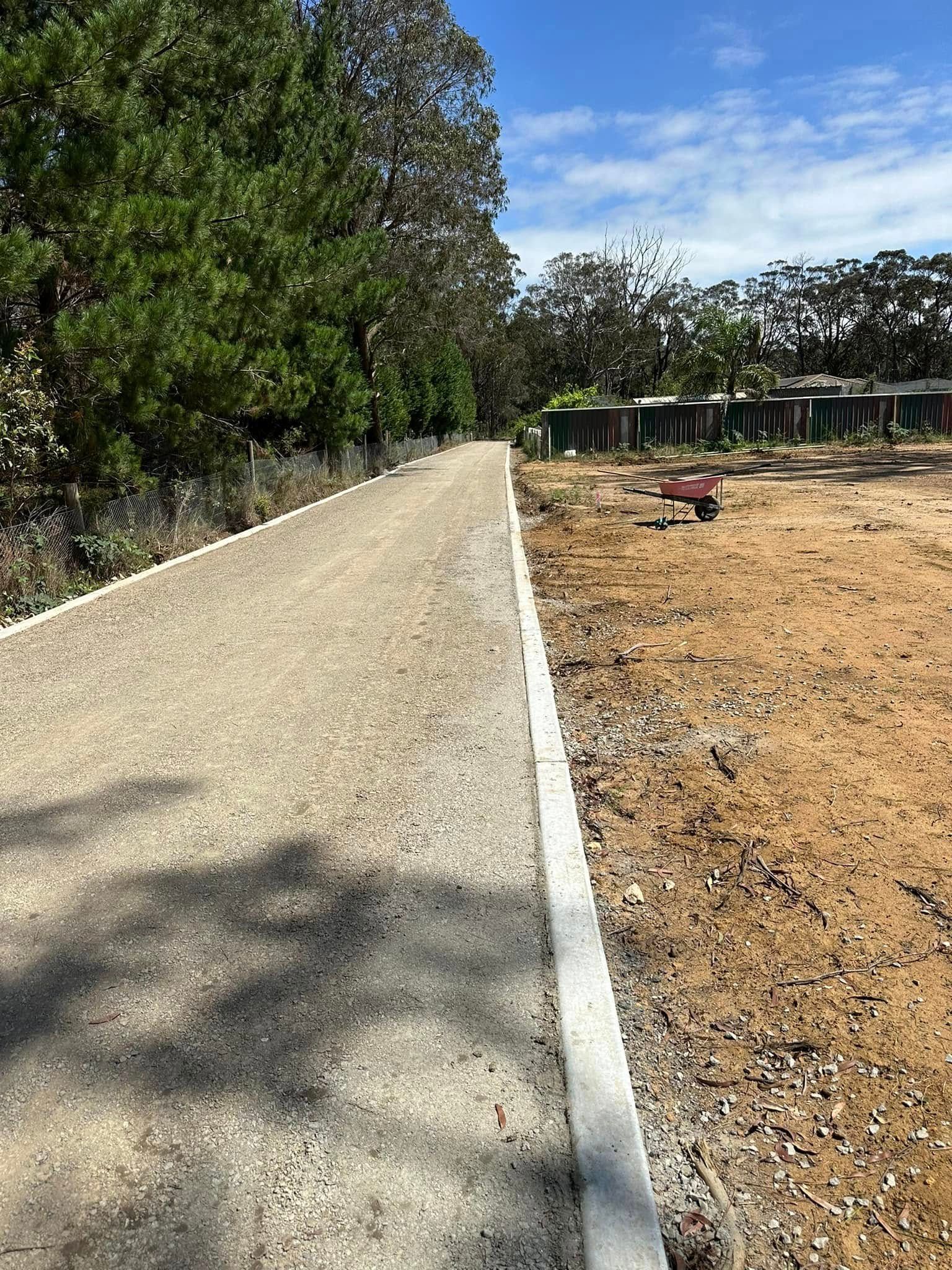 Paved path beside a dirt lot and trees on a sunny day