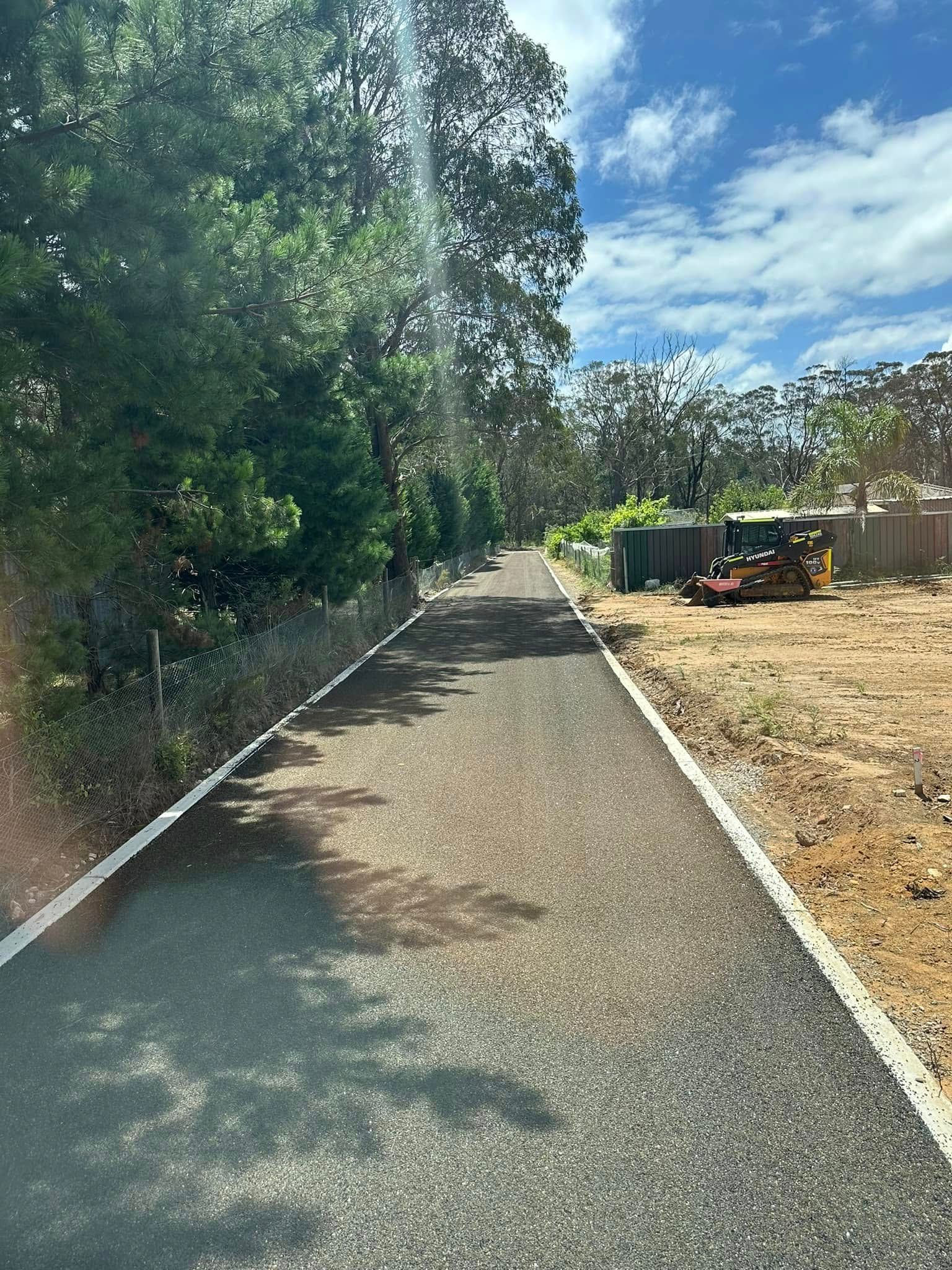 Tree-lined gravel path beside a wooden fence under a blue sky