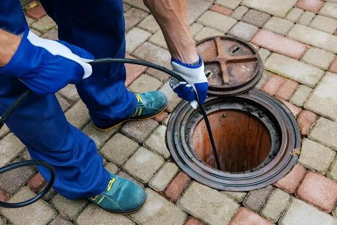 Worker opening a manhole on a paved walkway with a metal cover and inspection cable