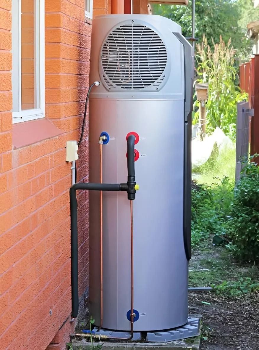 Tall silver outdoor tank with red and blue valves beside a brick wall and greenery