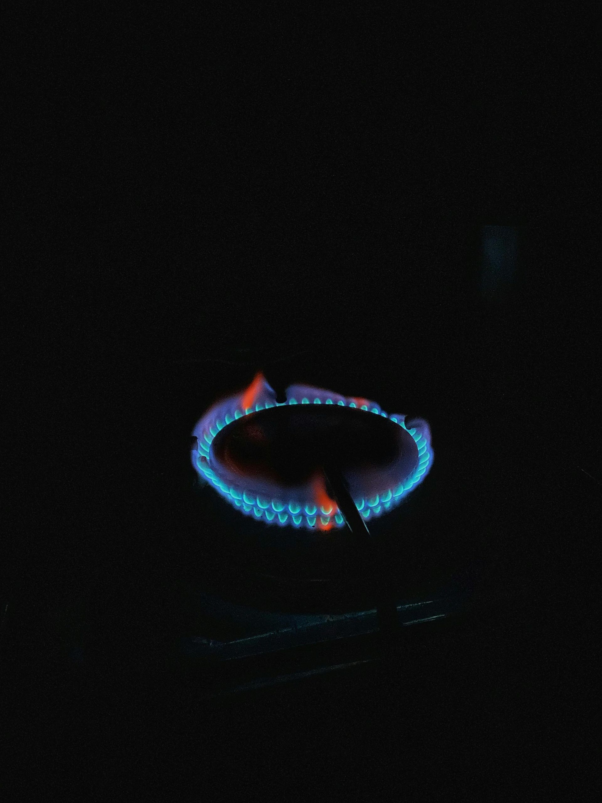 Blue gas burner flame in a dark setting, forming a glowing ring with orange highlights