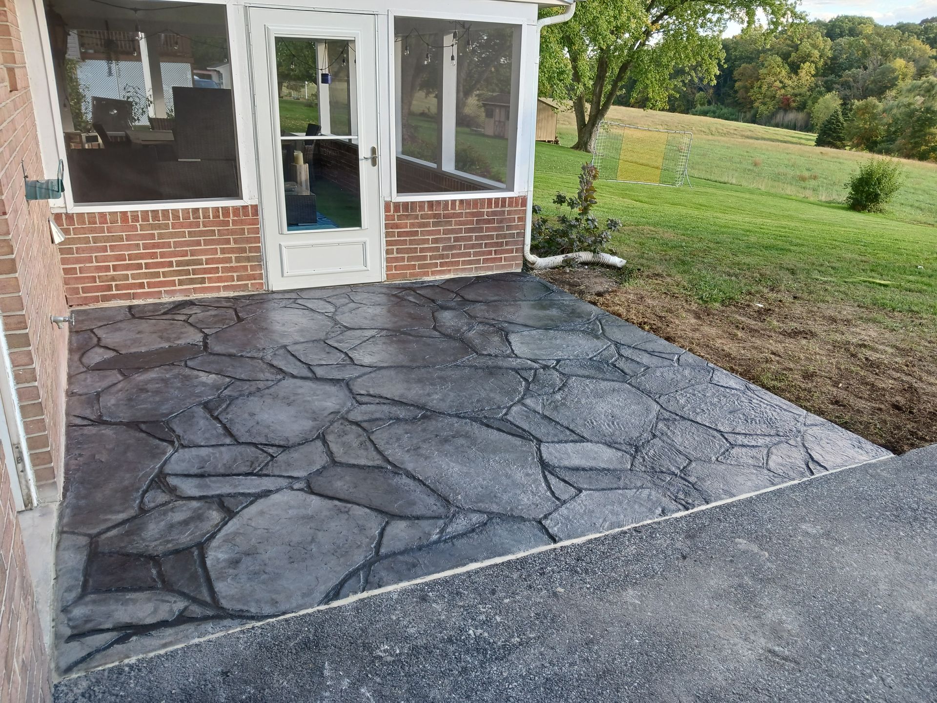 Patio with stamped concrete in a stone pattern; brick wall and screened porch in the background.