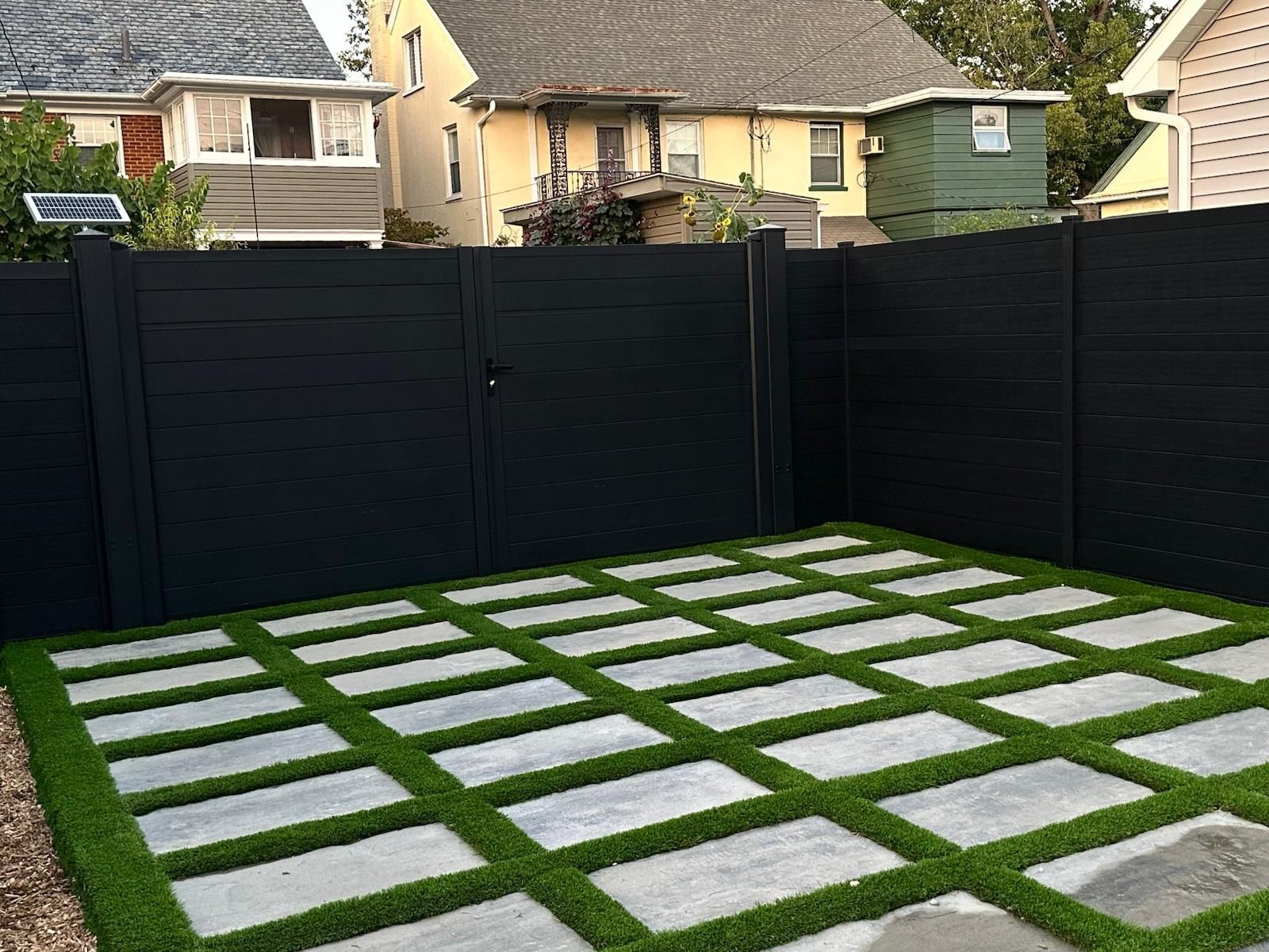 Black fenced backyard with concrete pavers set in green turf.