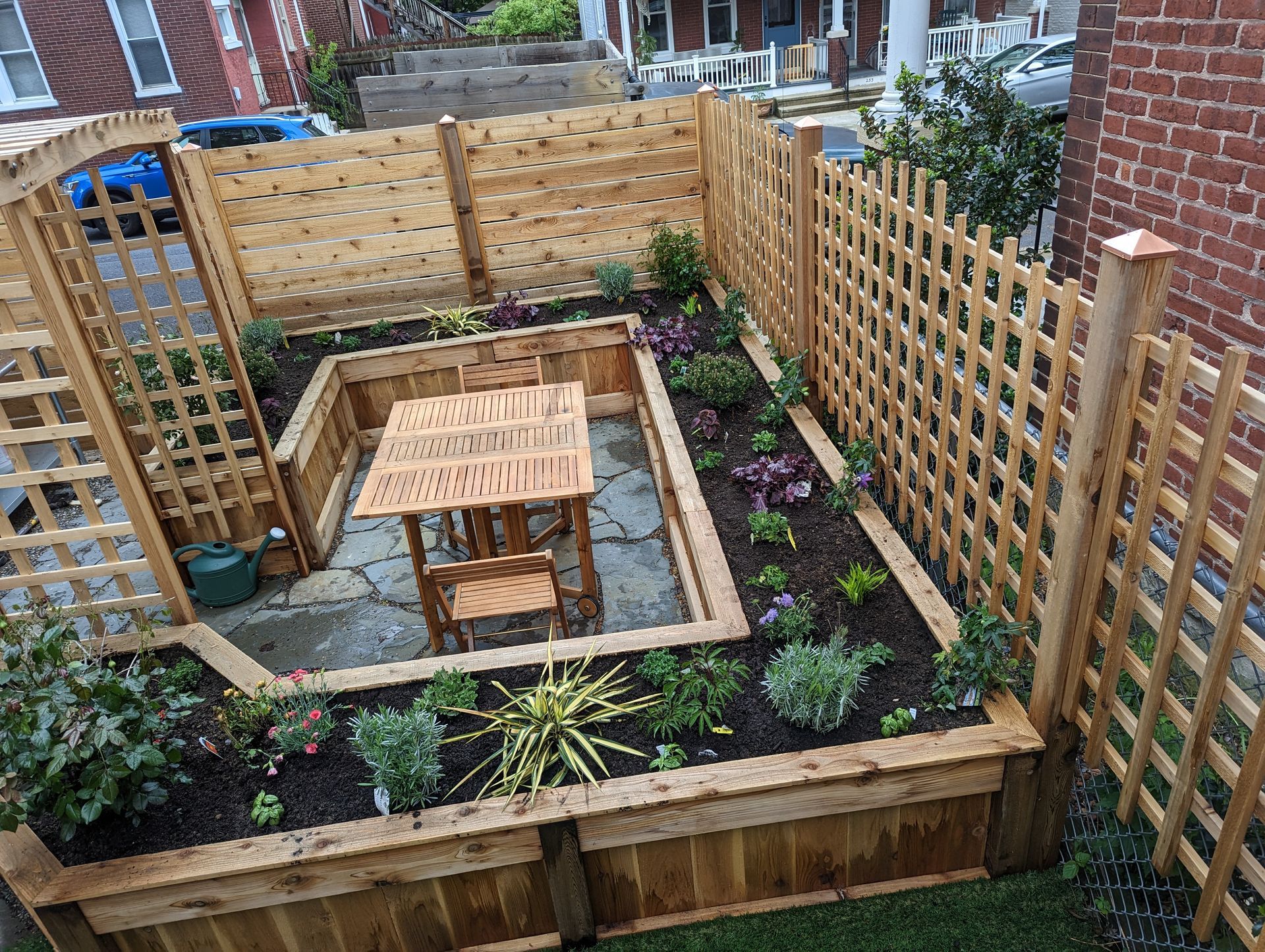 A small wooden garden with a table and chairs, enclosed by a trellis fence.