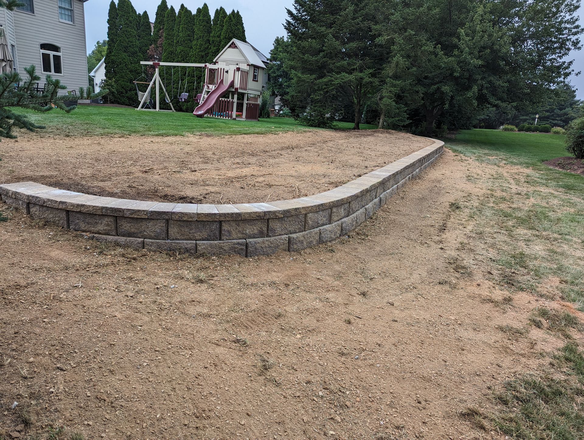Stone retaining wall with a graded yard and play set in the background.