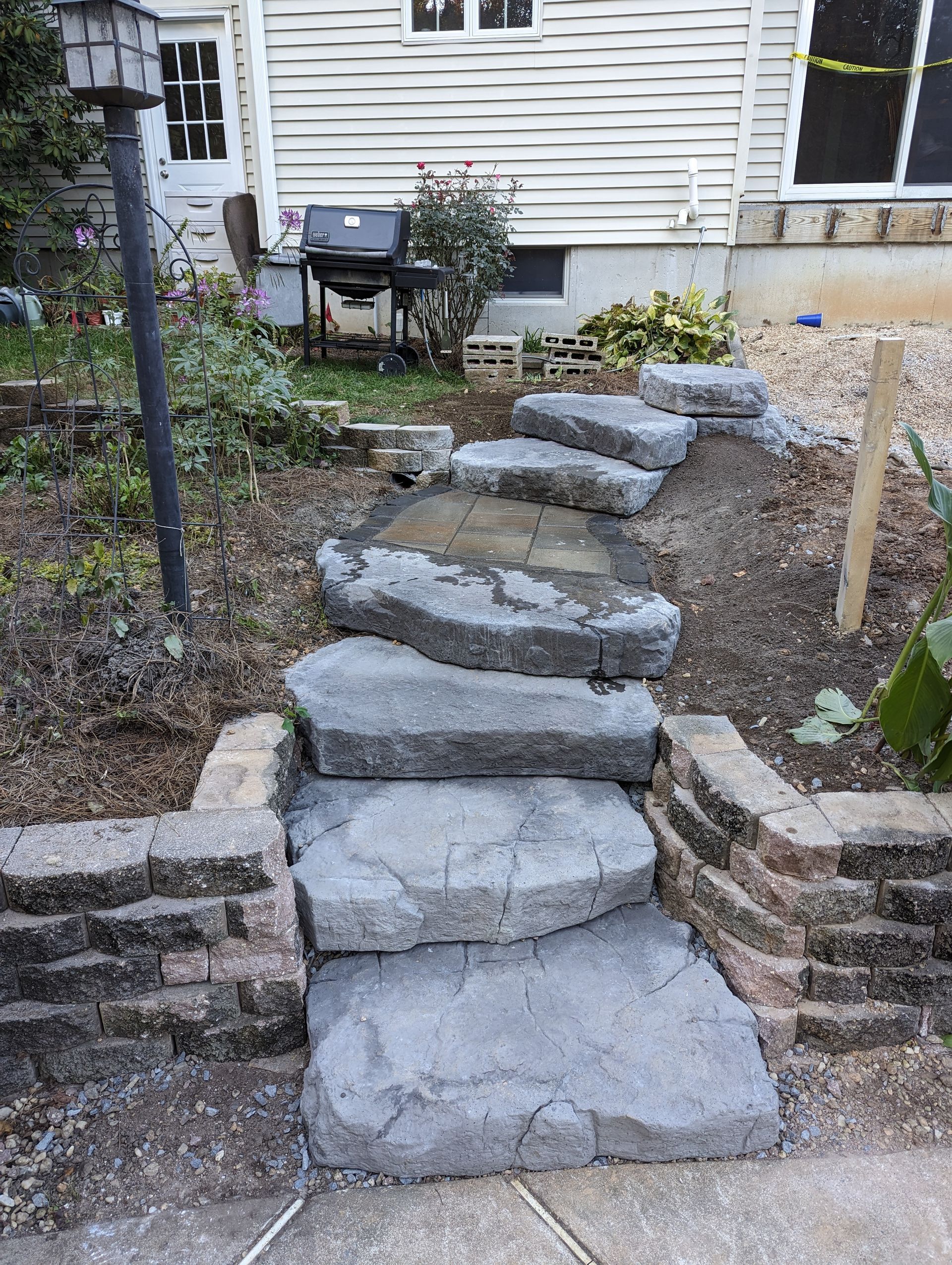 Stone steps leading up a garden path next to a brick retaining wall and a white house.