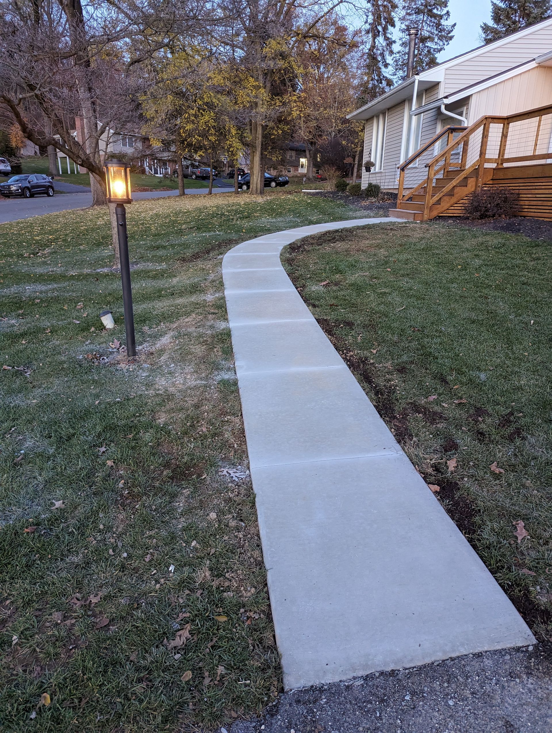 Concrete walkway curves through grass toward a house with a wooden porch.