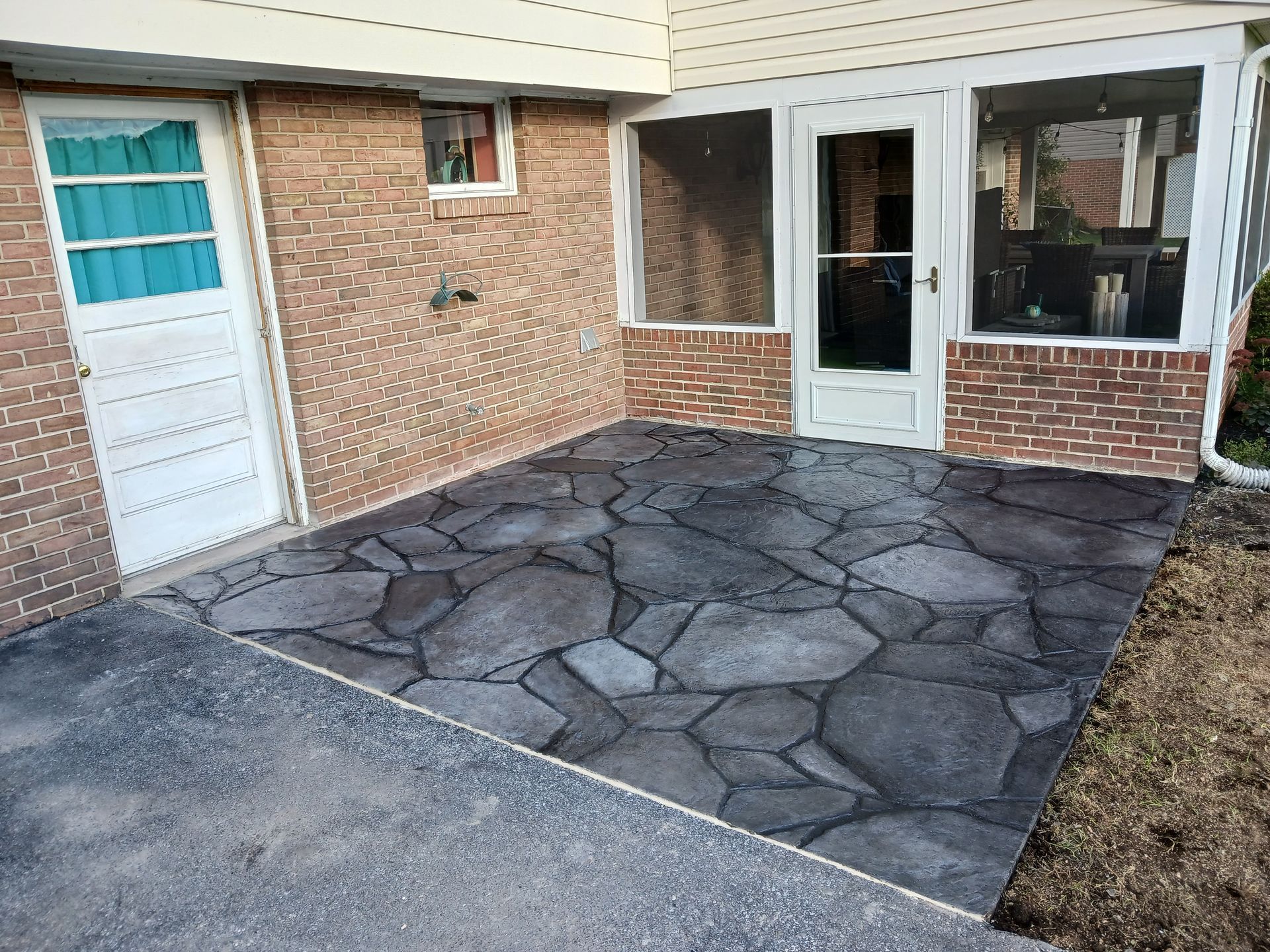 Patio with gray stone-like pattern, next to brick wall, door, and screened-in porch.