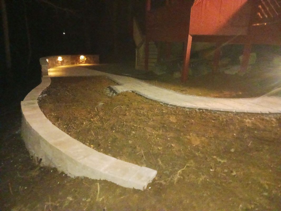 Concrete pathway and retaining wall curving through a dark yard, illuminated by small lights.
