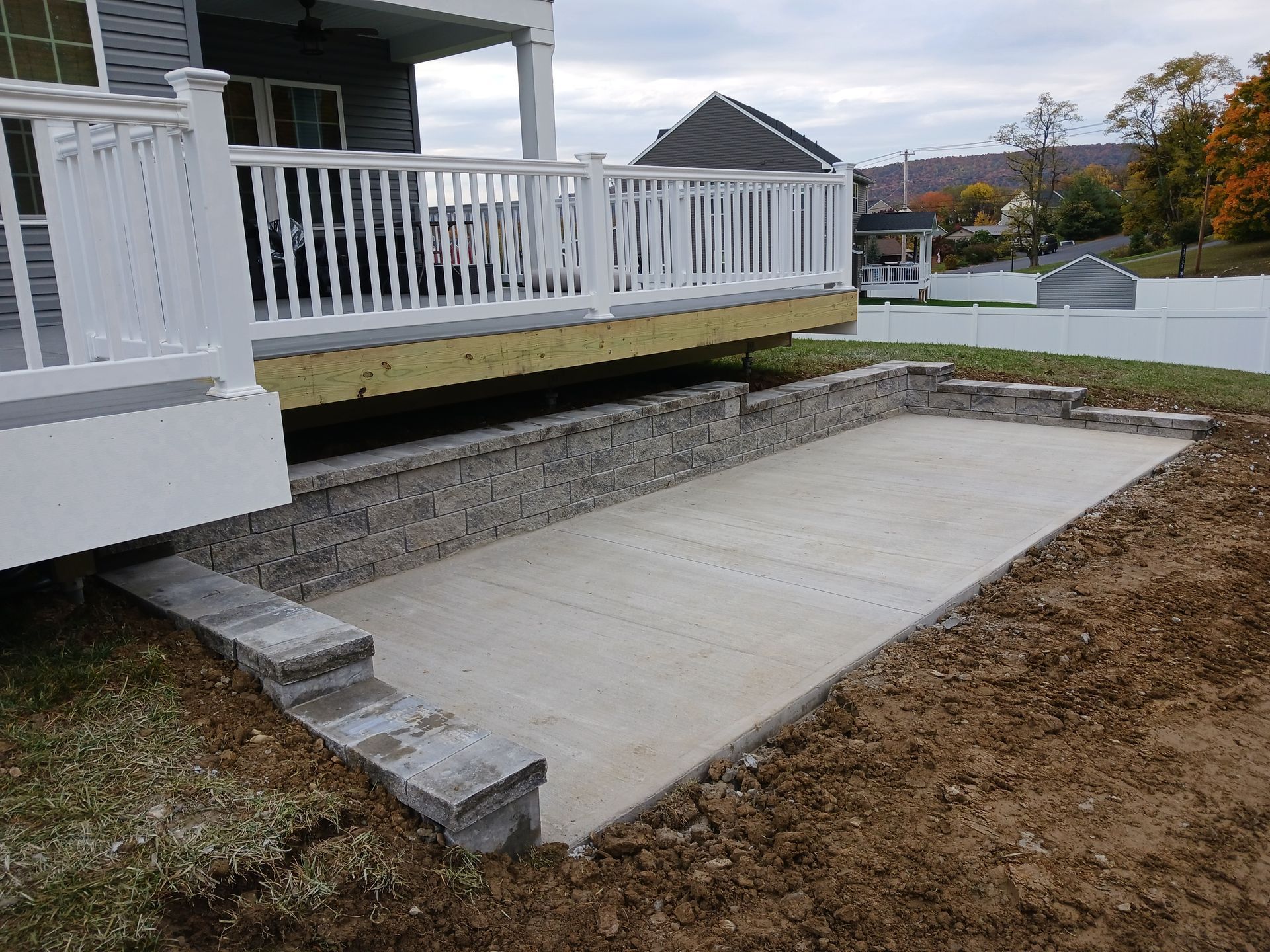Concrete patio below a white deck, with retaining wall and steps.