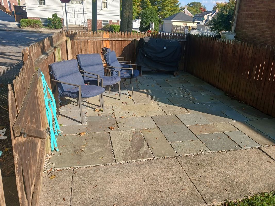 Small outdoor patio with blue chairs and a covered grill, enclosed by a wooden fence.
