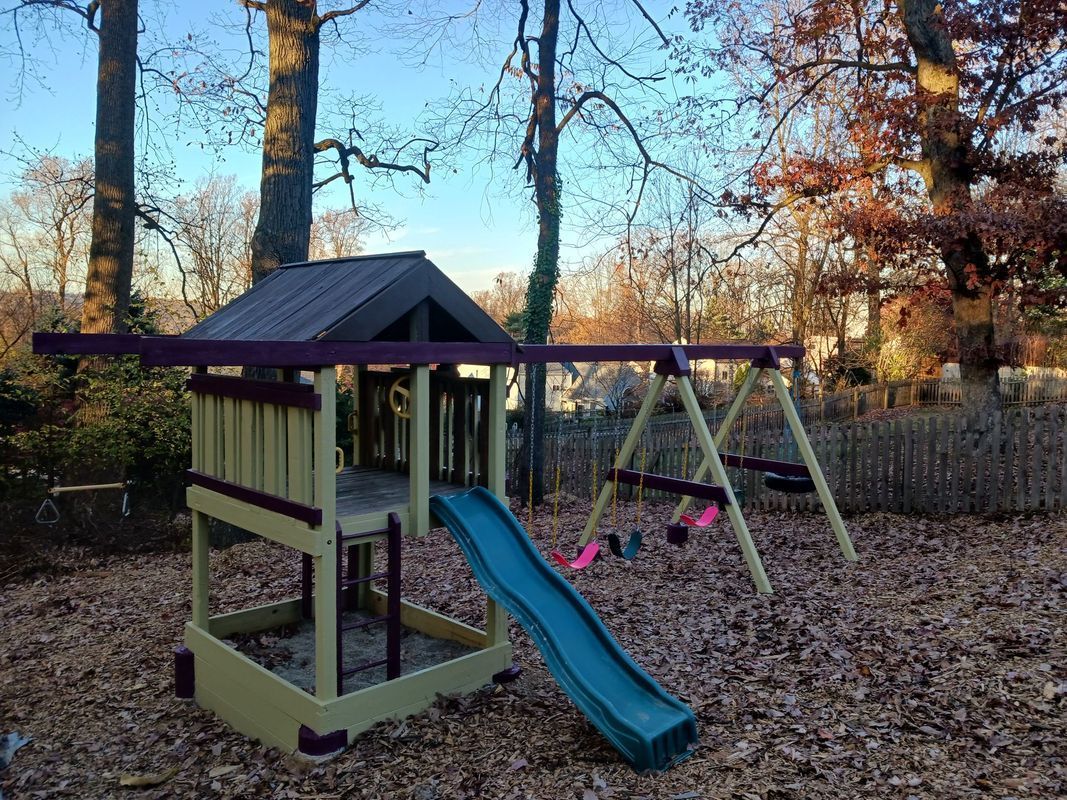 Playground set with a slide and swings in a yard covered in fallen leaves.