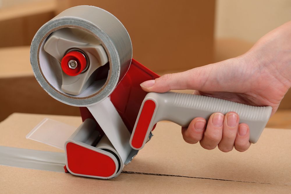 A person is holding a tape dispenser over a cardboard box.  — Town & Country Removals In Bonny Hills, NSW