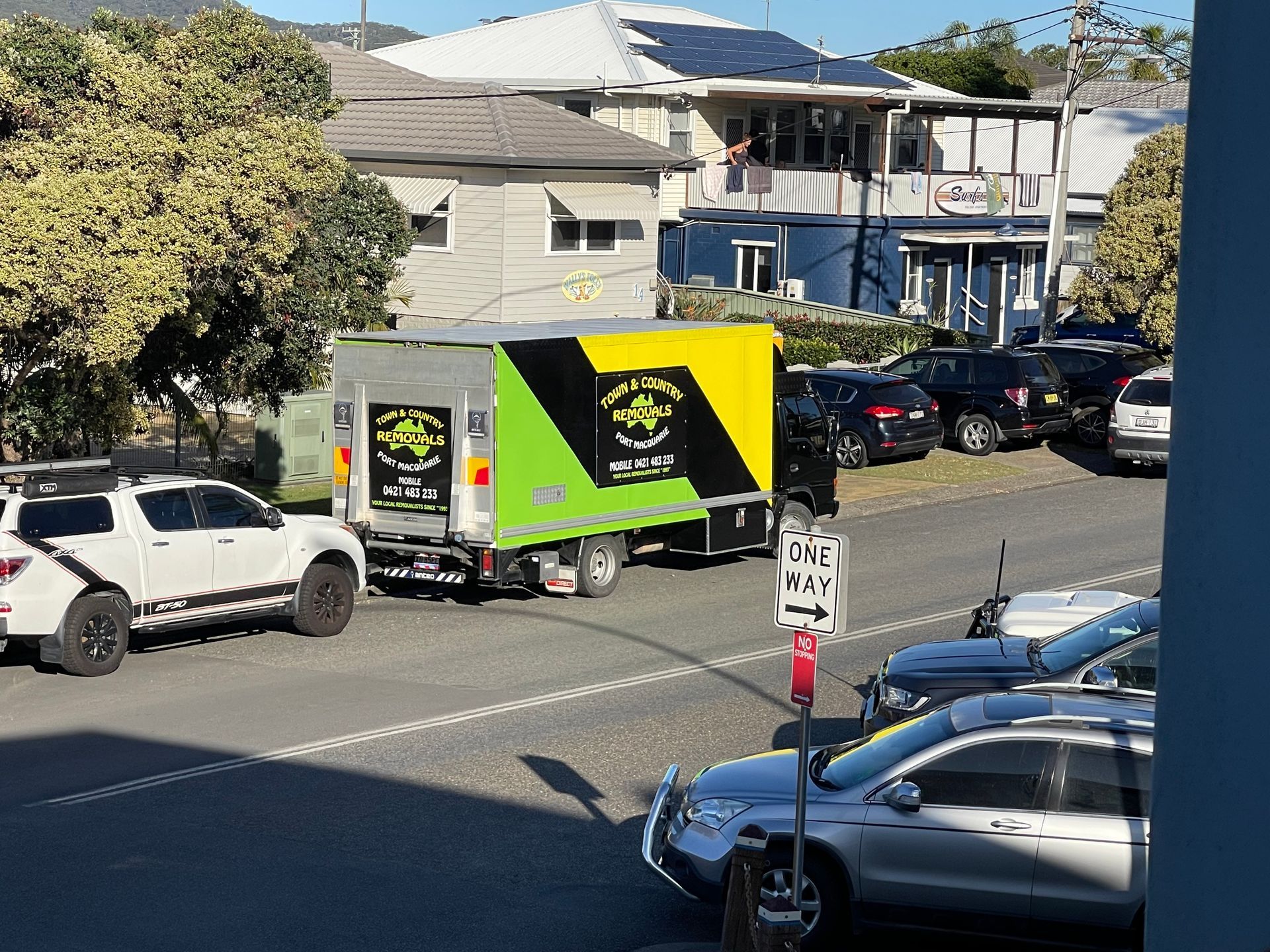 A Green and Yellow and Black Moving Truck Parked on a Busy Street  — Town & Country Removals In Thrumster, NSW