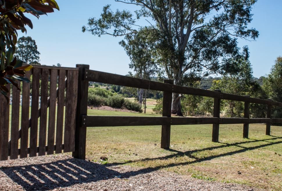 A Wooden Fence Surrounds a Grassy Field With Trees in the Background — Town & Country Removals In Thrumster, NSW