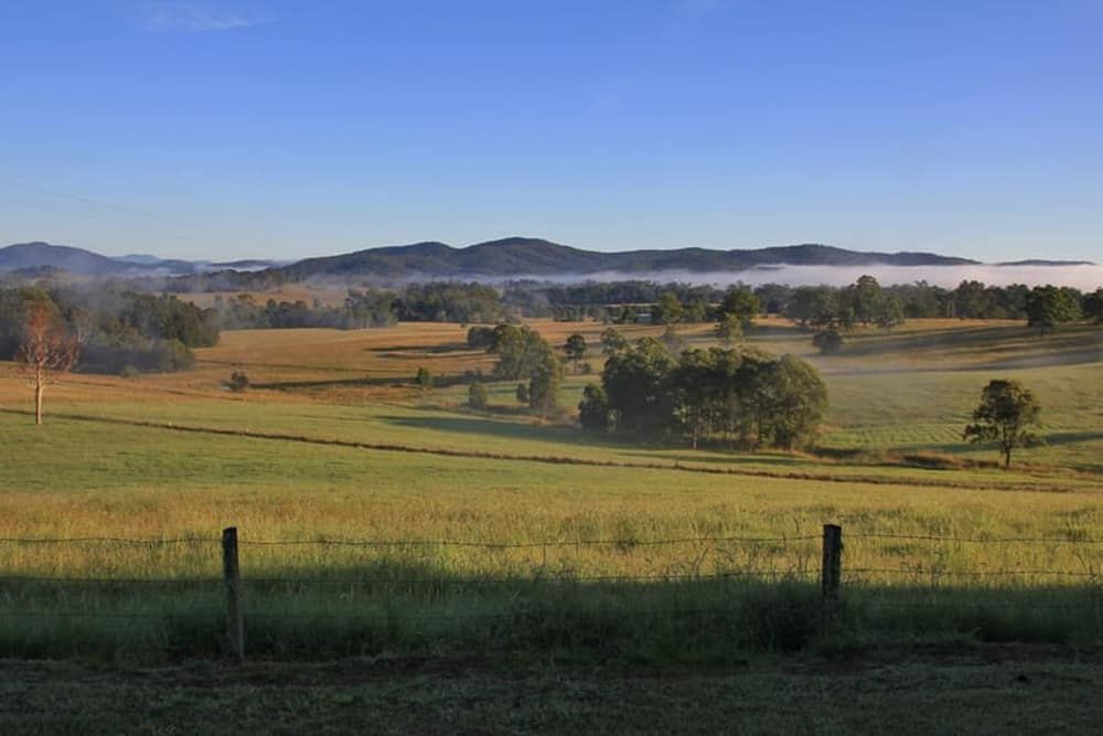 A Fence Surrounds a Grassy Field With Mountains in the Background — Town & Country Removals In Wauchope, NSW
