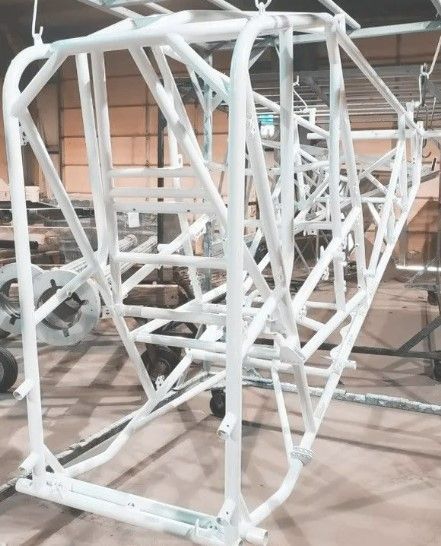 White powder-coated roll cage frame, presumably for a vehicle, in a workshop setting.