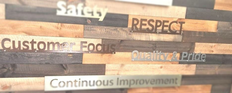 Text on a wooden wall: Safety, Respect, Customer Focus, Quality & Pride, Continuous Improvement.