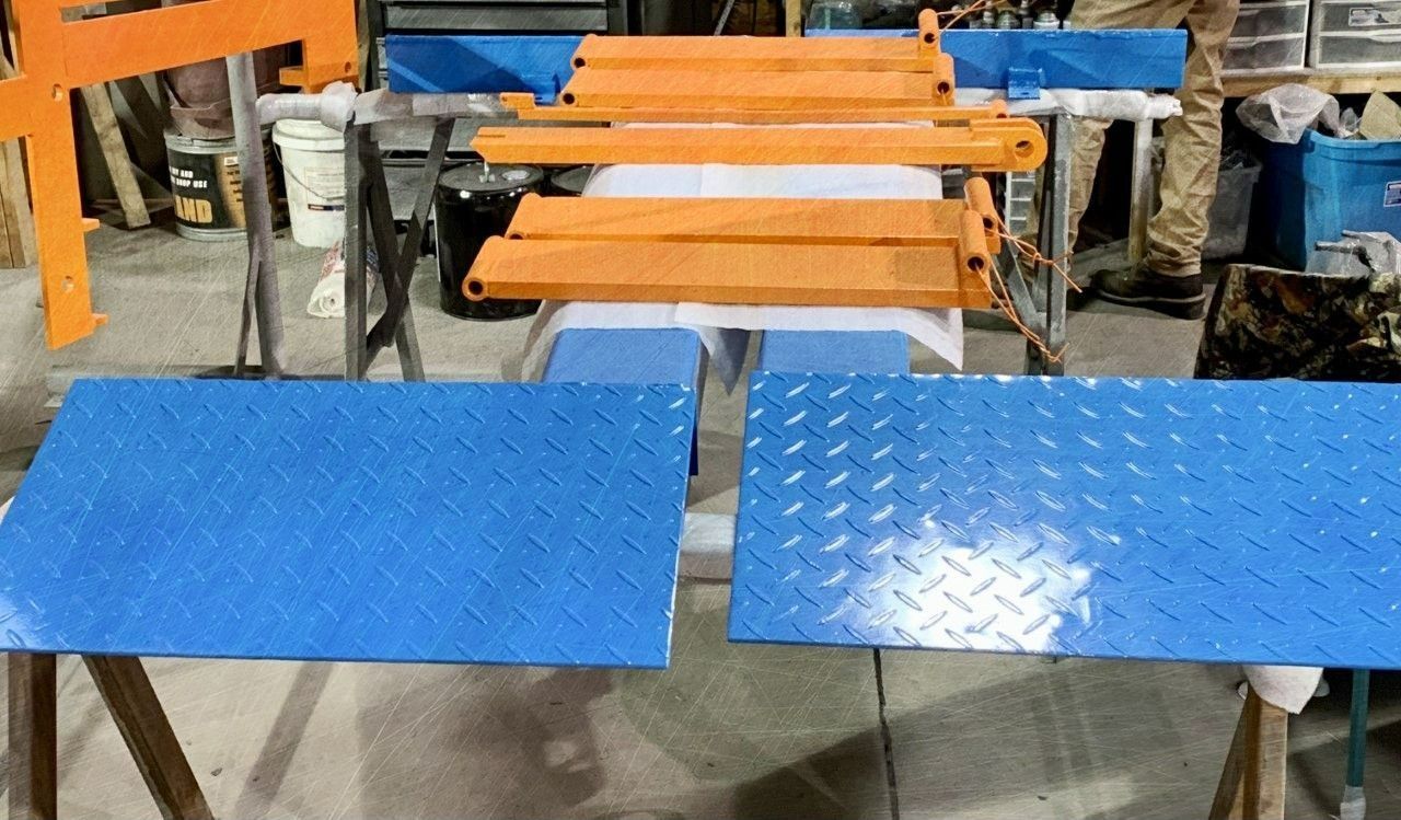 Blue and orange painted metal pieces on sawhorses in a workshop.