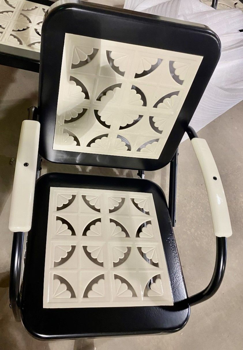 Black metal chair with cream geometric design on seat and back, white armrests.