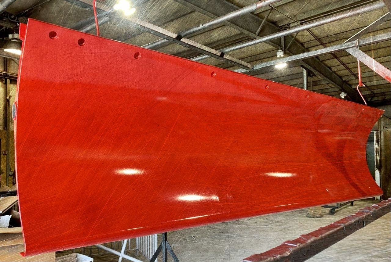 Red snowplow blade hanging in a workshop.