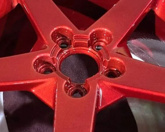 Red metallic five-spoke car wheel with circular lug nut holes.