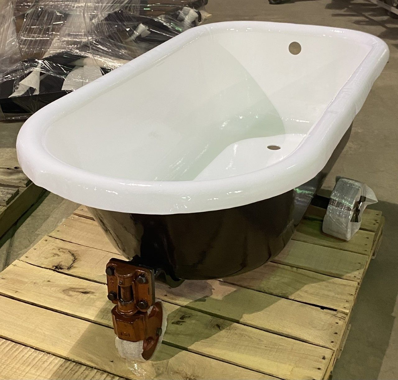 Clawfoot bathtub with white interior, brown exterior, and antique-style faucet, on a wooden pallet.