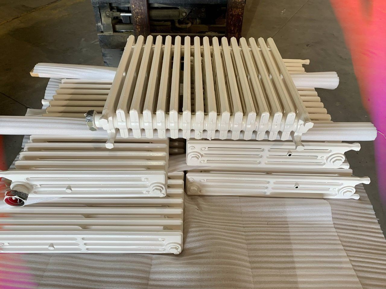White cast iron radiators stacked on a pallet in a warehouse setting.