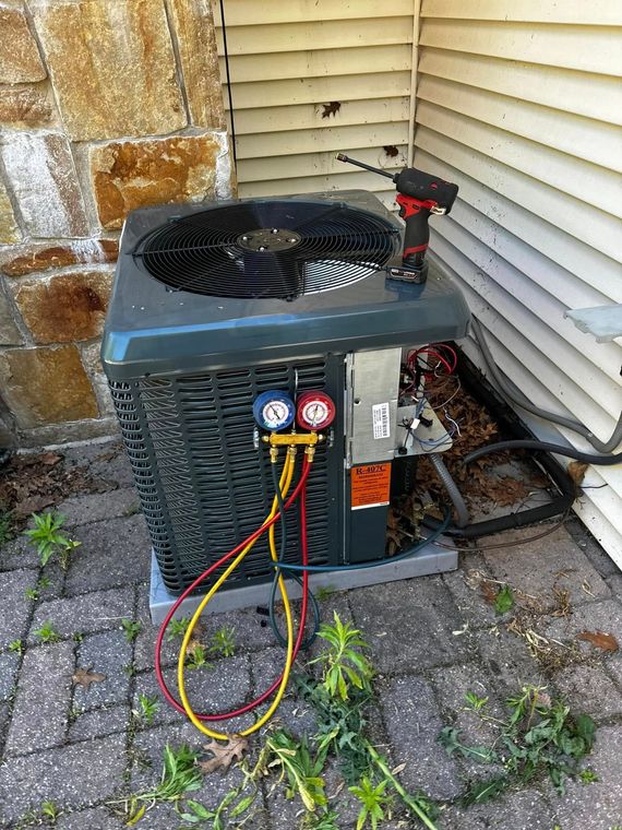 Outdoor HVAC unit with gauges and hoses attached beside a house wall