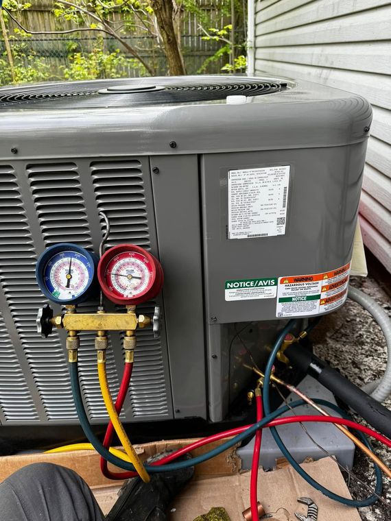 Outdoor HVAC unit with blue and red gauges attached to service ports and hoses on the side panel