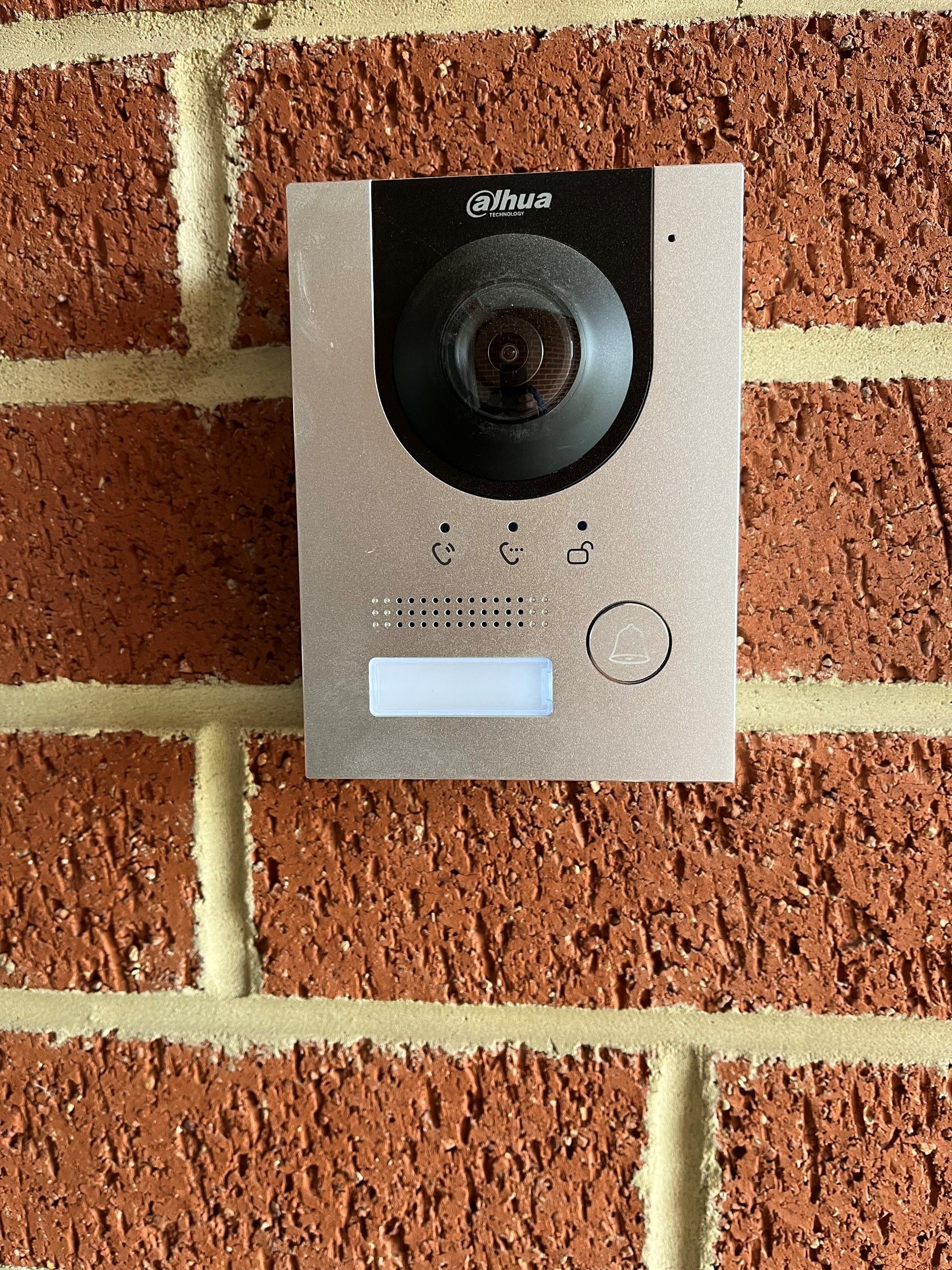 Silver doorbell with a camera, mounted on a red brick wall.
