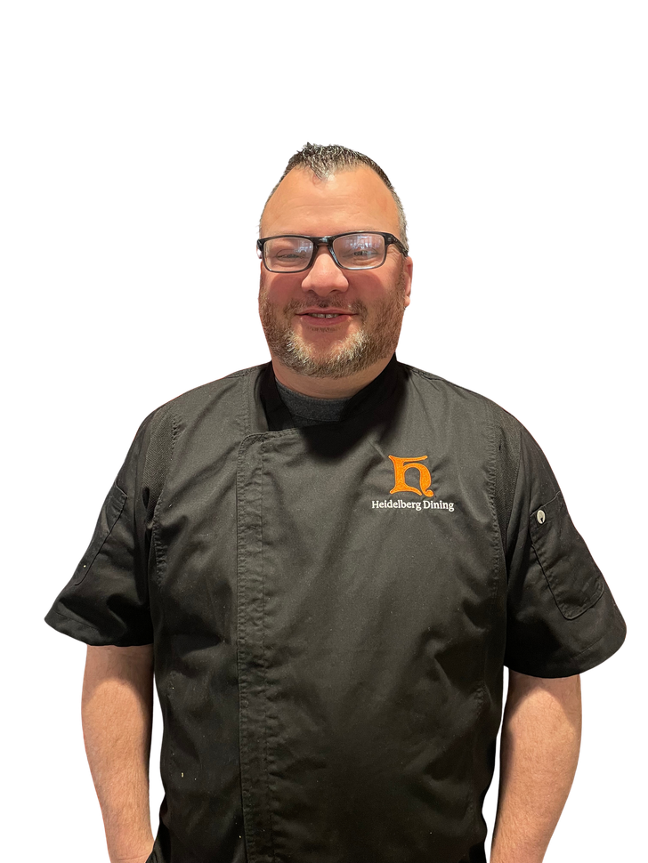 A chef in a black uniform with a Parkhurst logo smiling.