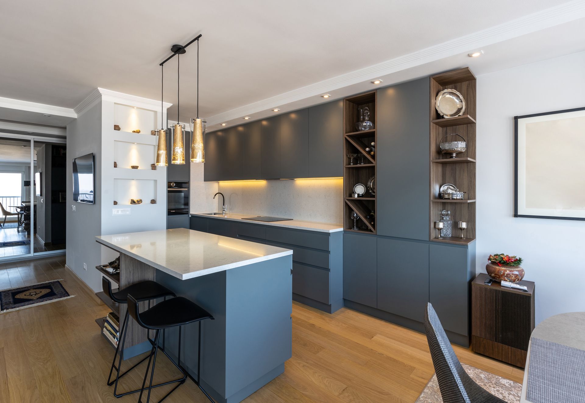 Modern kitchen with gray cabinetry, white countertops, island with bar stools, and pendant lights.