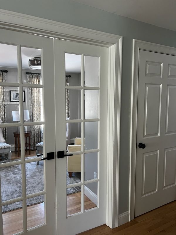 A hallway with white french doors leading to a living room.