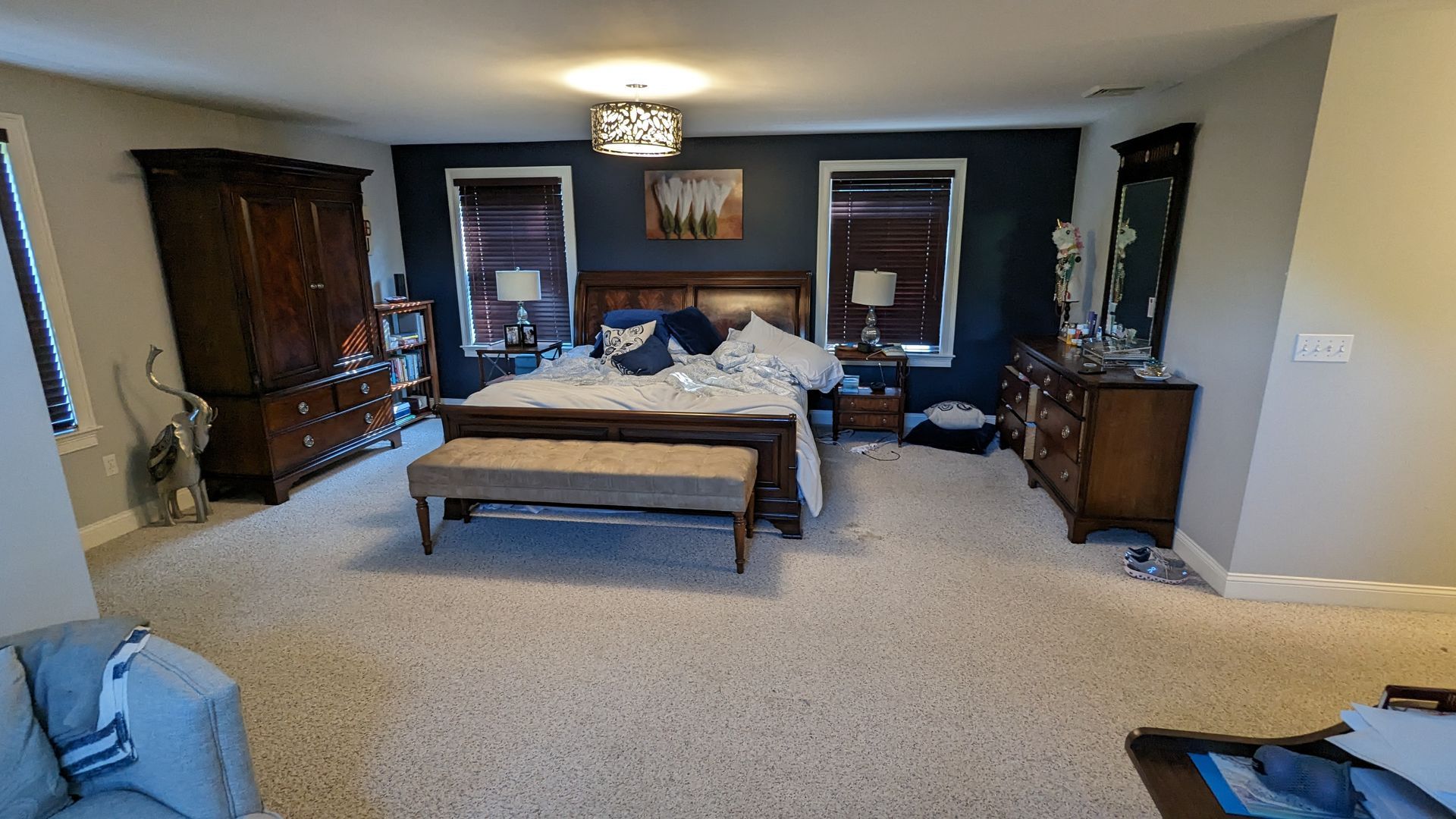 A bedroom with a king size bed , dresser , mirror and bench.