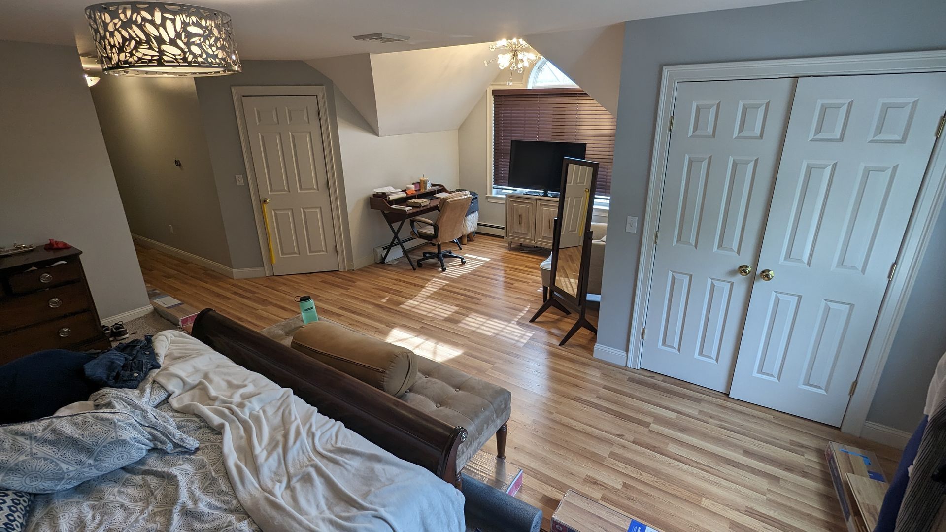 A bedroom with a bed , dresser , desk , television and closet.