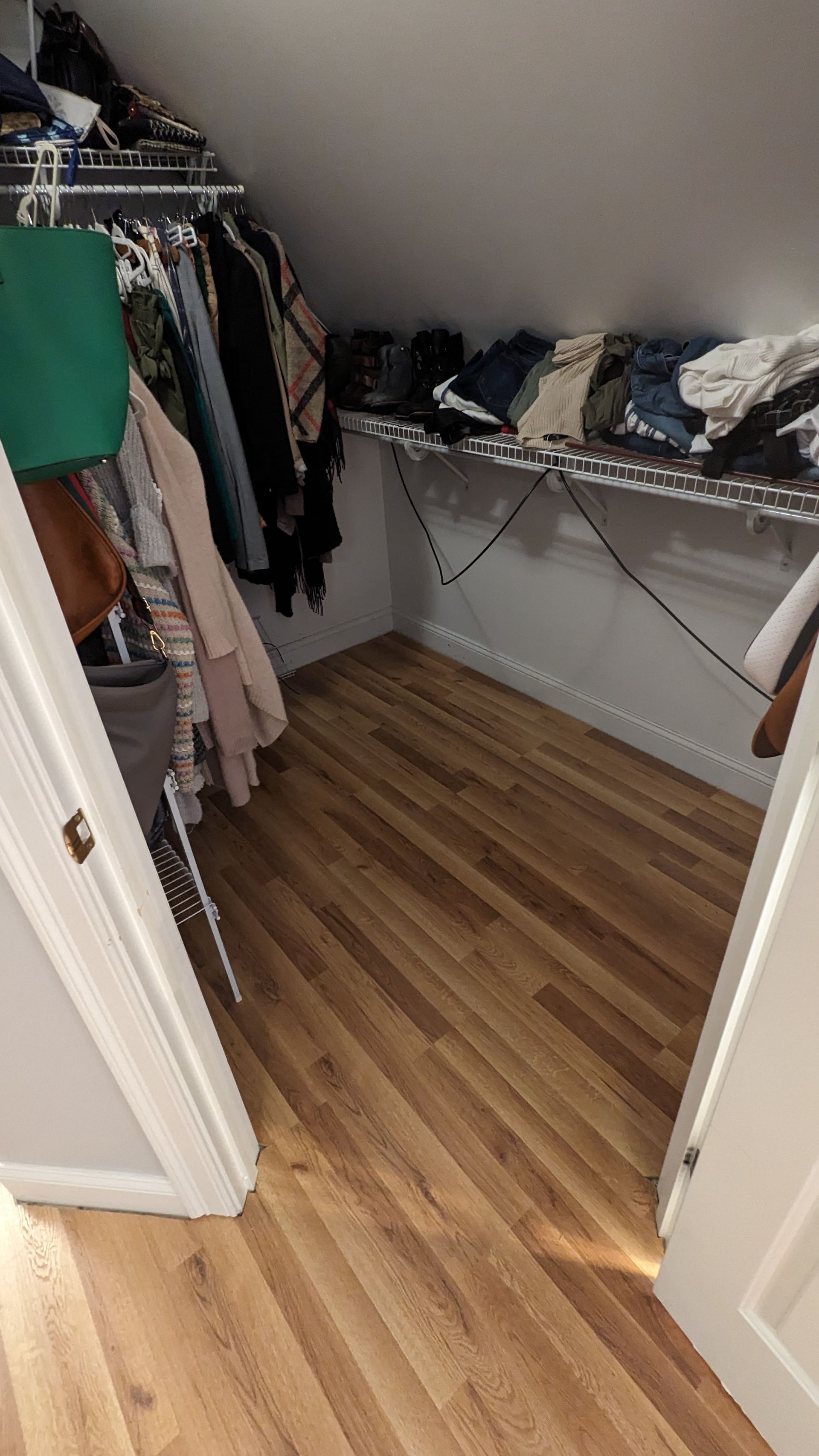 A walk in closet with a slanted ceiling and wooden floors.