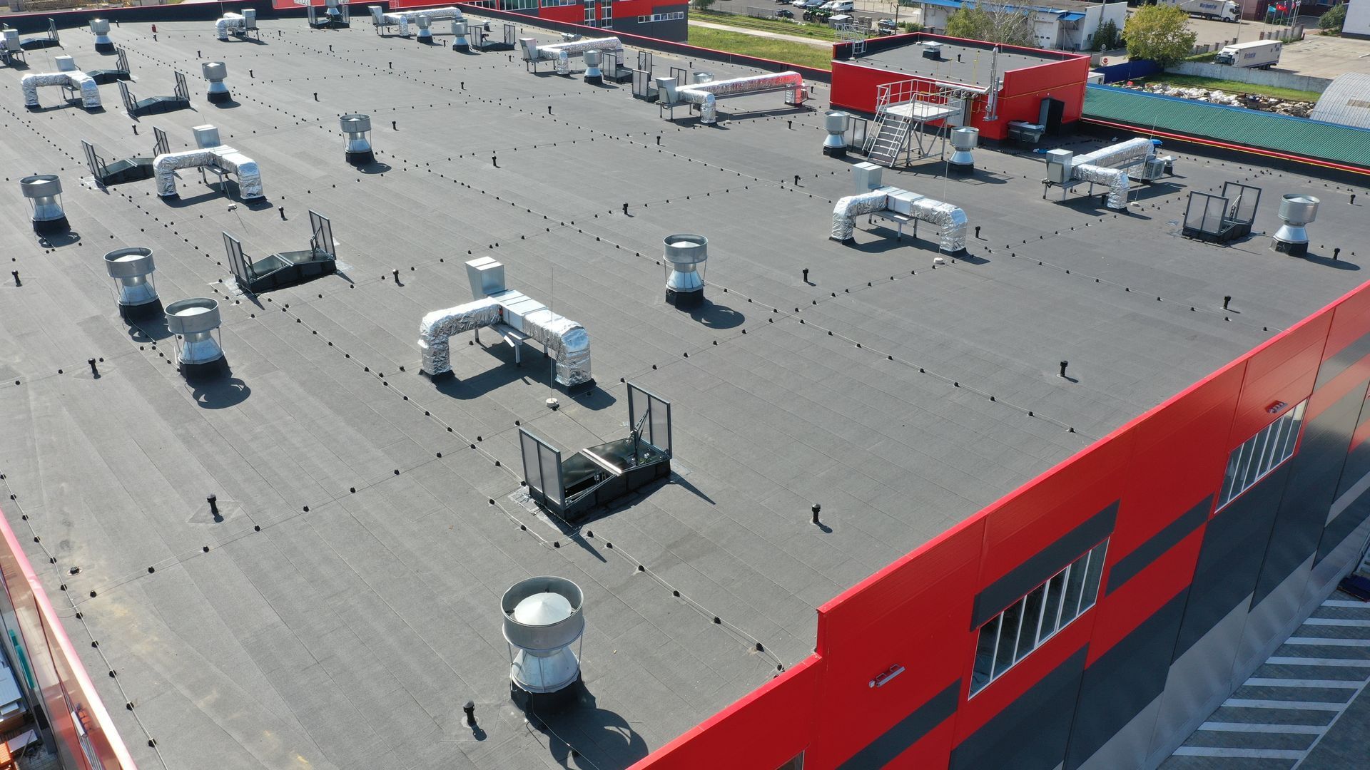Rooftop view with HVAC units and vents atop a red industrial building under bright sunlight