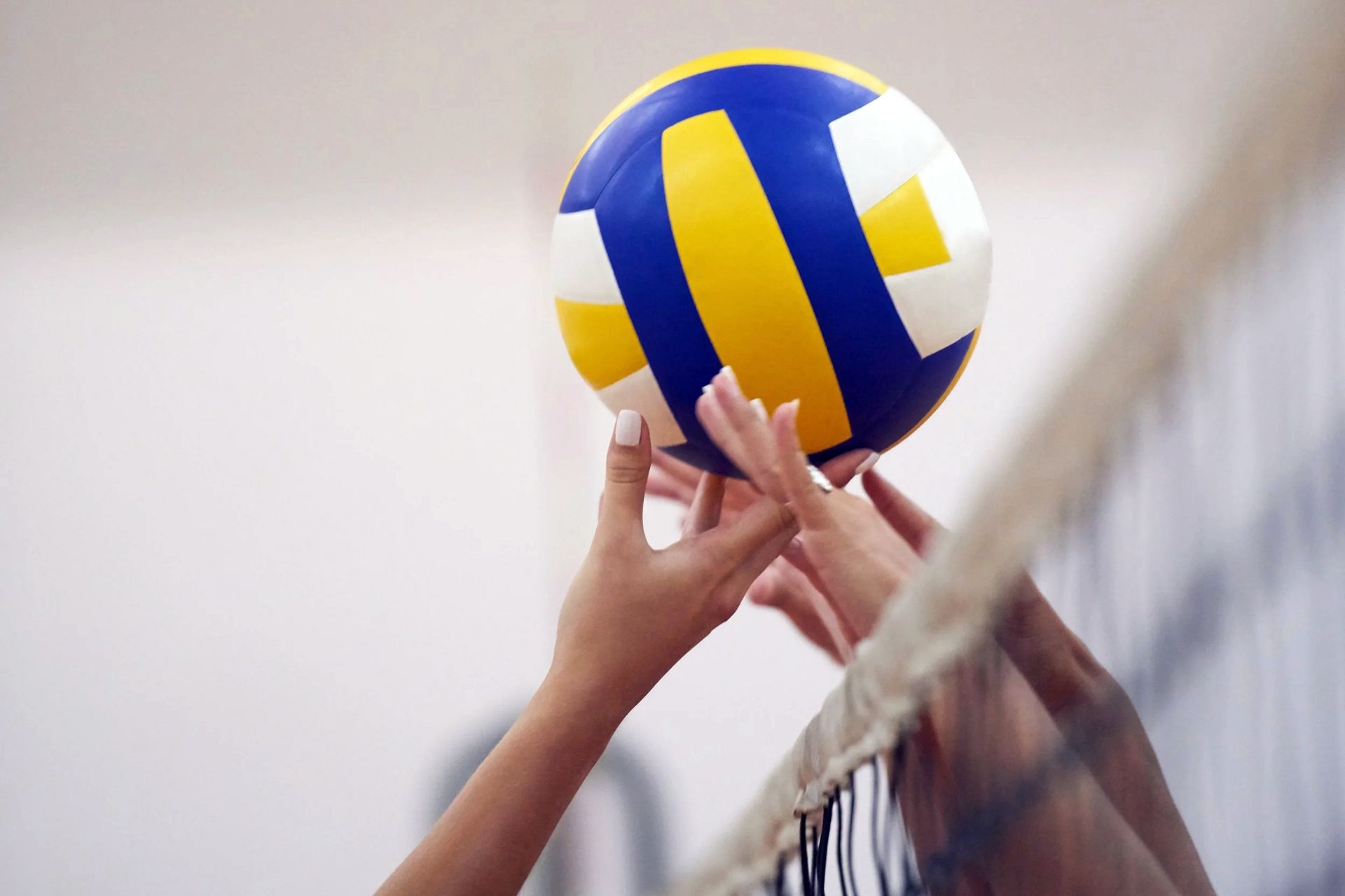 Mani che posizionano un pallone da pallavolo blu, giallo e bianco sopra la rete