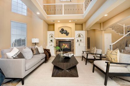 Spacious beige living room with high ceilings, fireplace, gray sofa, and modern coffee table.