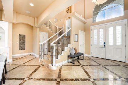 Bright foyer with marble floors, curved staircase, and double front doors in a beige home.