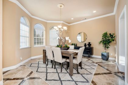 Bright dining room with a wooden table, upholstered chairs, arched windows, and a large rug.