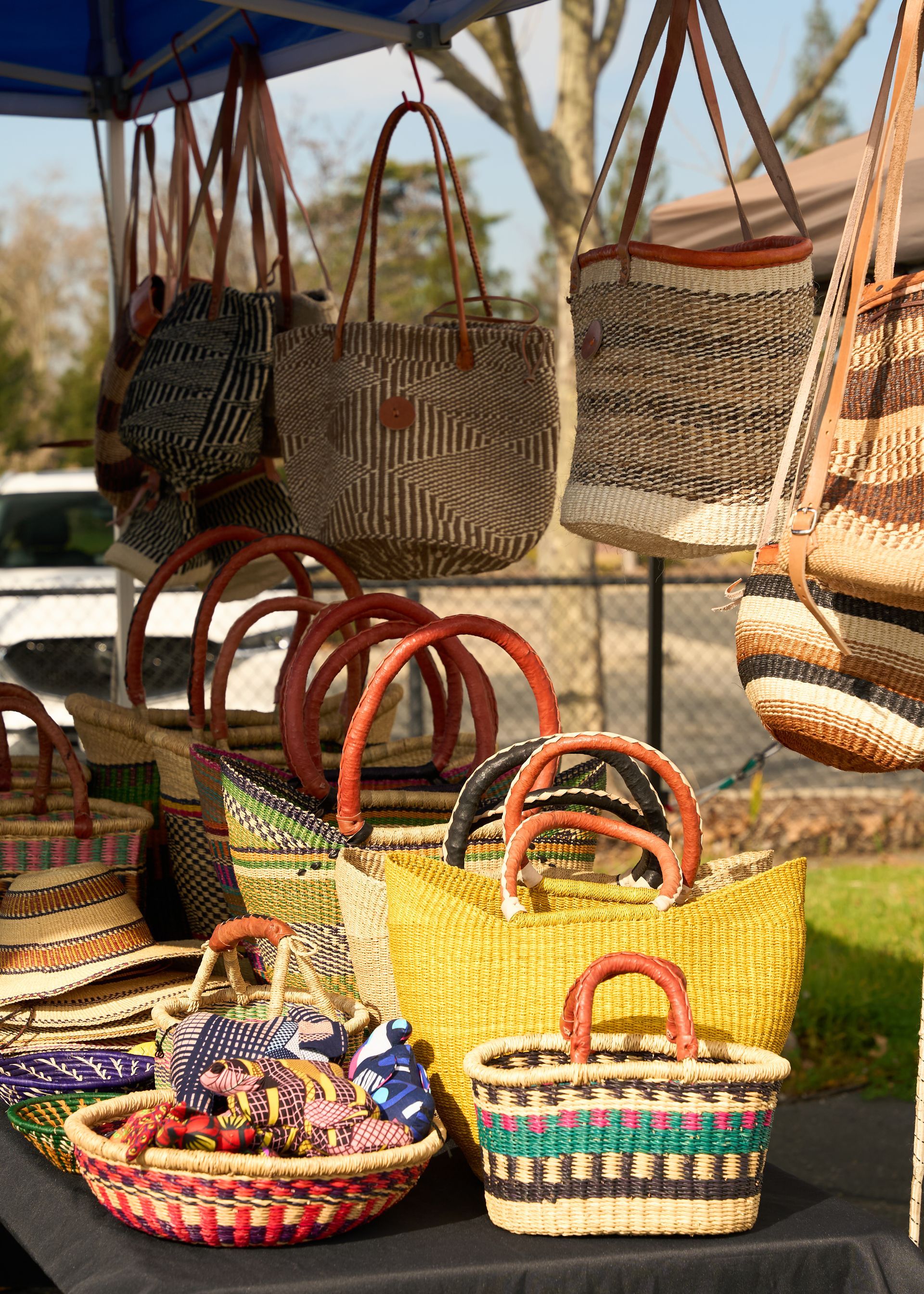 Handwoven wicker baskets with colorful handles displayed outdoors at a market stall at the Loomis Community Farmers Market