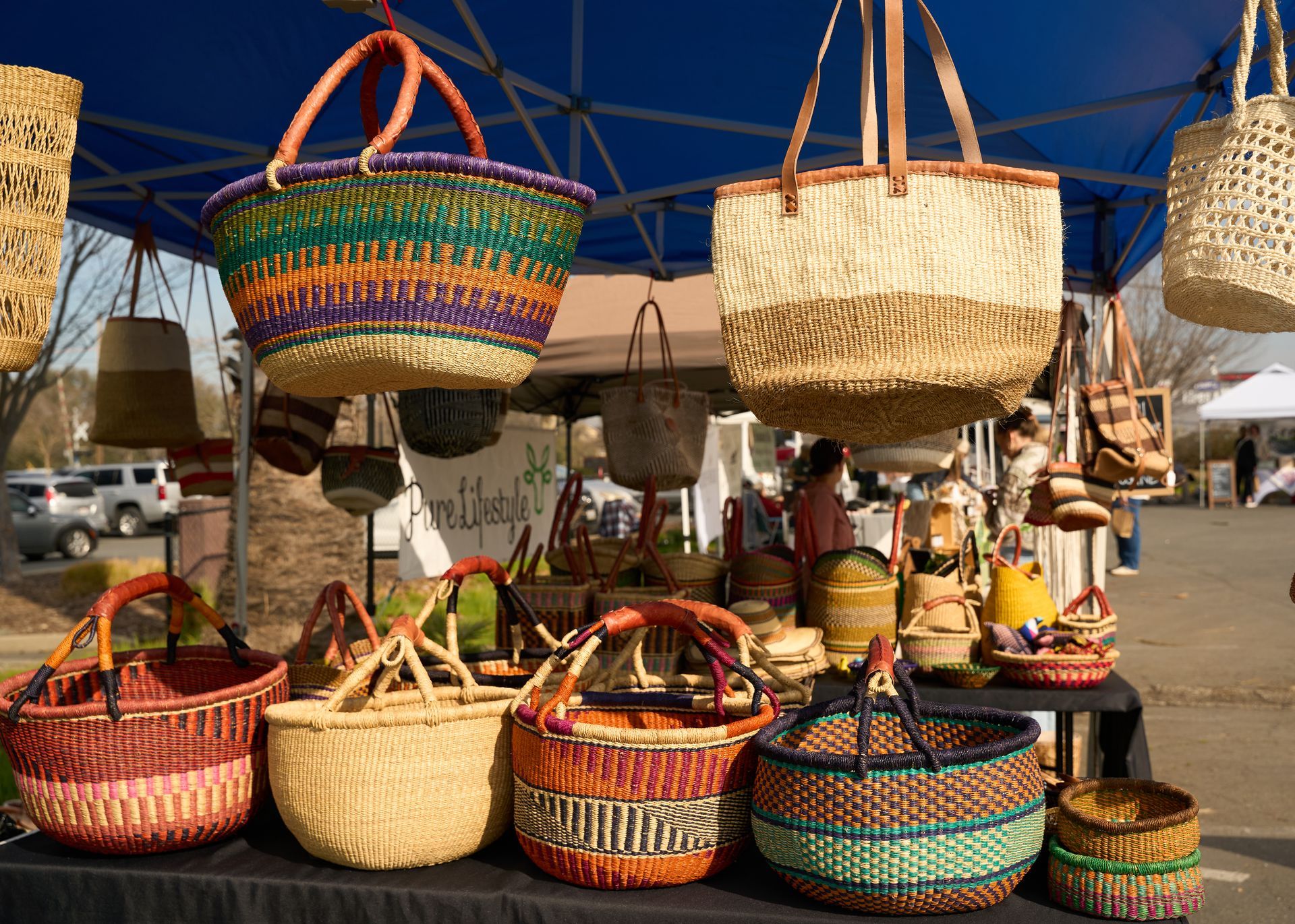 Colorful artisan woven baskets displayed at an outdoor vendor stall under a blue canopy tent at the Loomis Community Farmers Market