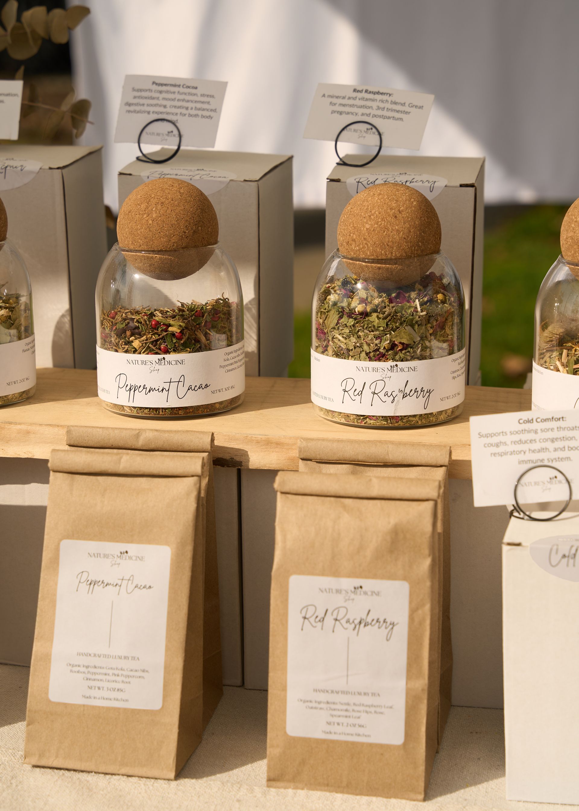 Artisan gift jars with cork tops and brown paper bags displayed with decorative greenery on a table at the Loomis Community Farmers Market