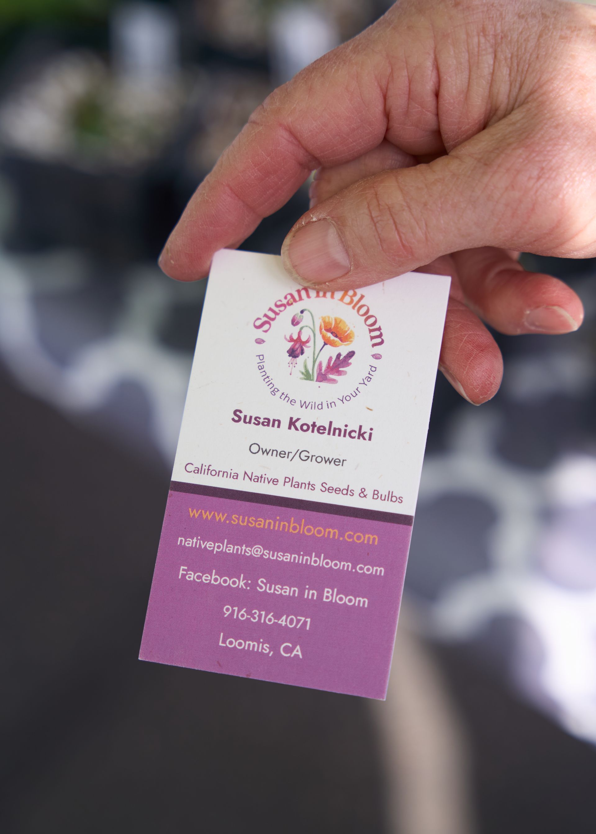 Hand holding a pink and white vendor business card against a soft blurred background at the Loomis Community Farmers Market