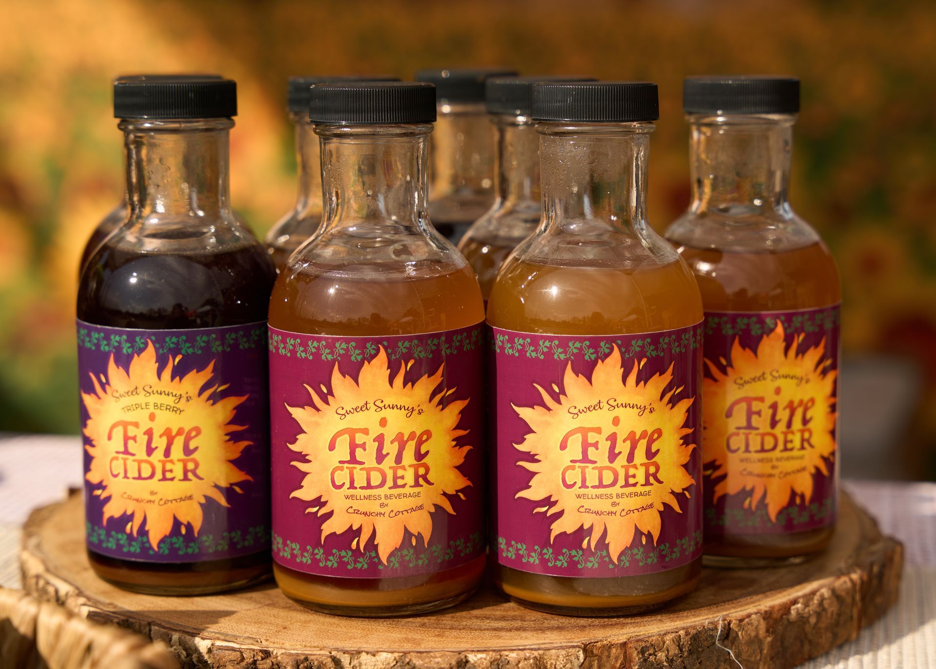 Four bottles of Fire Cider tonic with purple and orange labels and black caps displayed on a rustic wooden slab at the Loomis Community Farmers Market