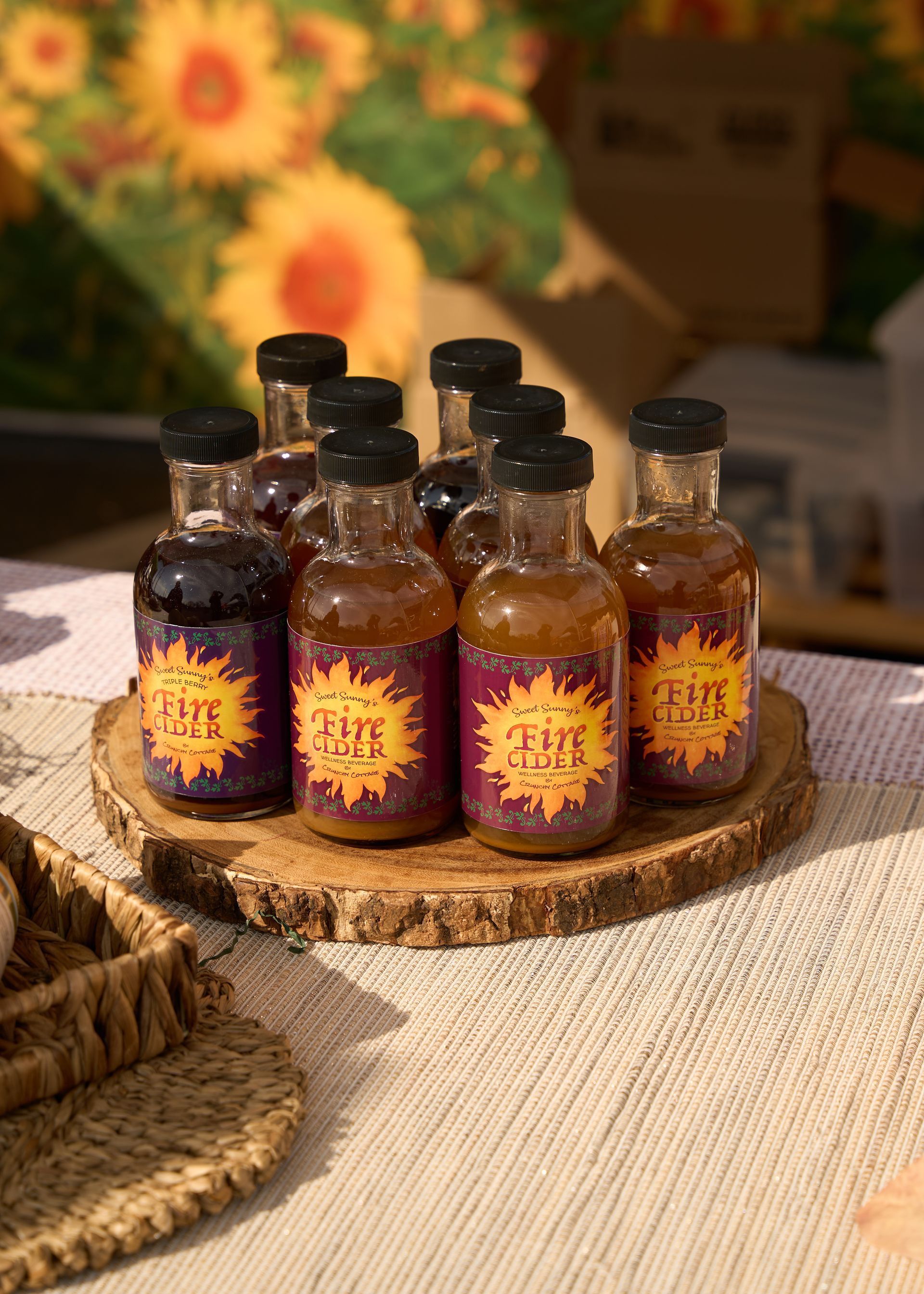 Small amber glass bottles with black caps and orange labels arranged on a woven tray in warm sunlight at the Loomis Community Farmers Market