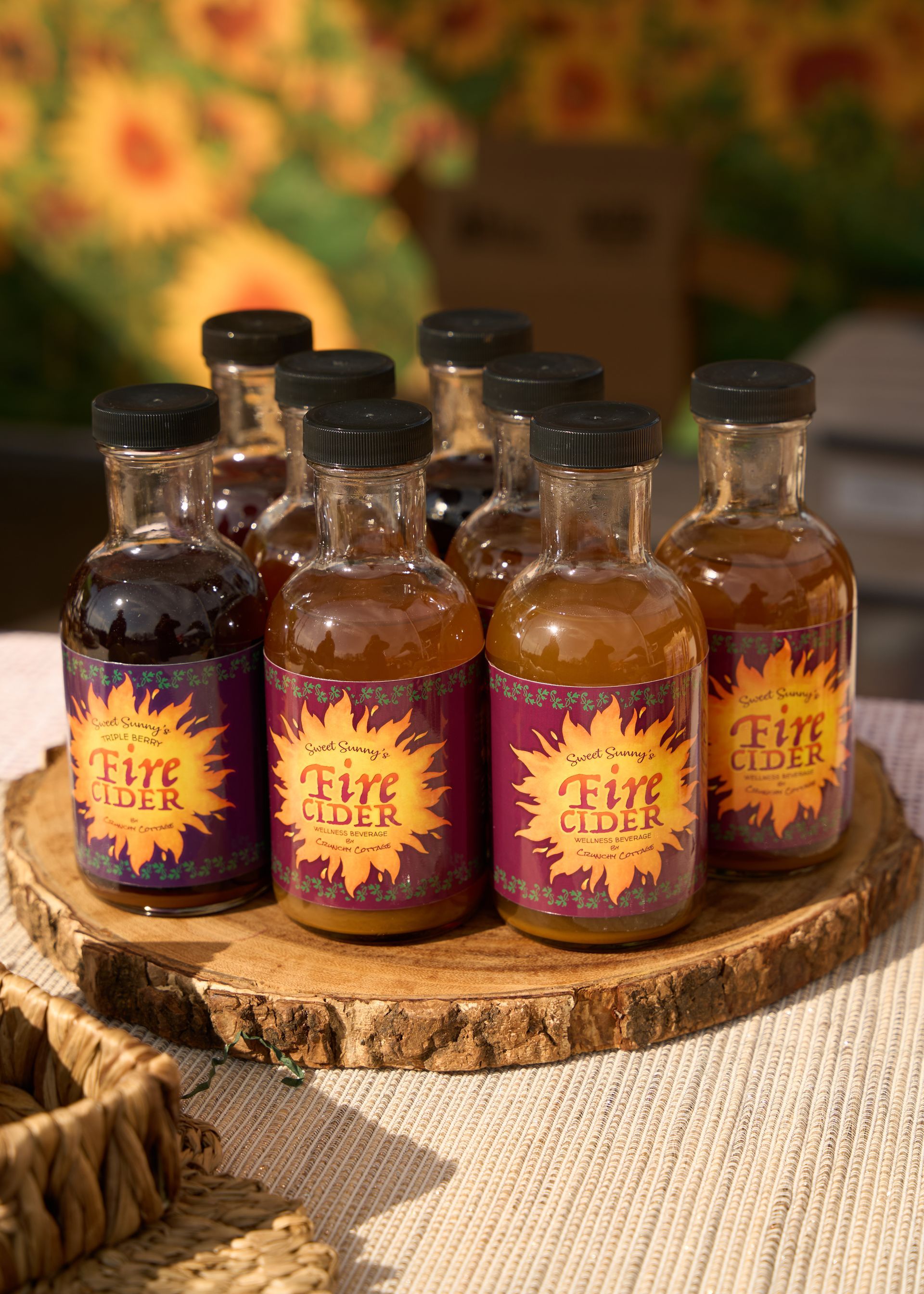 Small amber glass bottles with black caps and purple-gold labels displayed on a rustic wooden slab at the Loomis Community Farmers Market