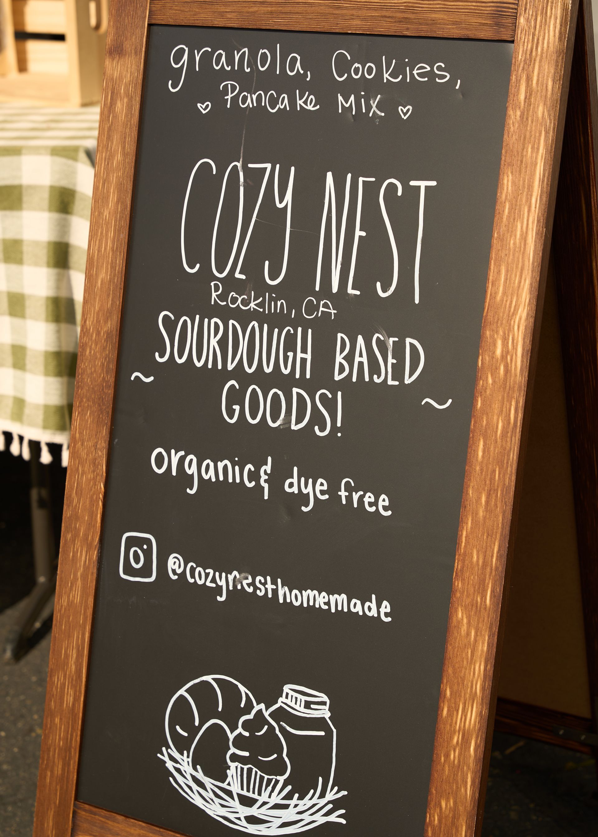 Chalkboard sign for Coy West sourdough goods listing fresh granola, cookies, and zinnia mix inside a rustic shop at the Loomis Community Farmers Market